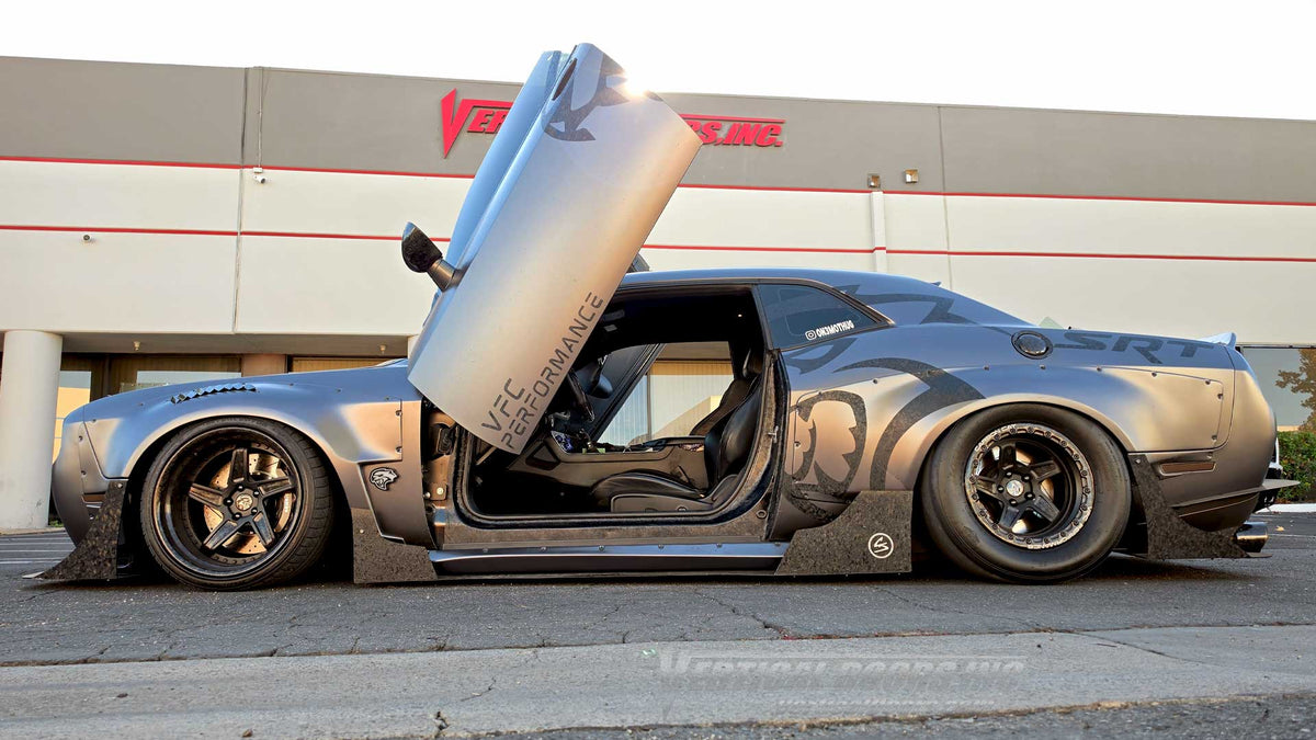 Driver-side profile of the Carbon Cat Dodge Challenger Hellcat with a raised vertical door, exposed hinge hardware, black interior, and riveted widebody fenders. VDCDCHAL08
