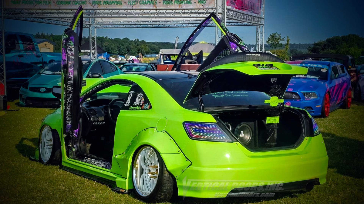 Rear three-quarter view of Kyle’s green widebody Honda Civic with both doors raised, multicolor taillights, and an open trunk displaying custom audio. - VDCHC06082D