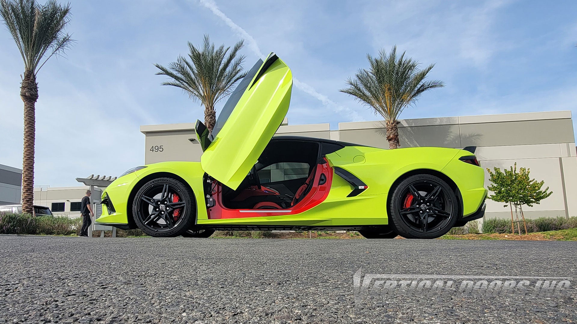 Lime green Corvette C8 with a raised vertical door, red-and-black interior, black wheels and red brake calipers