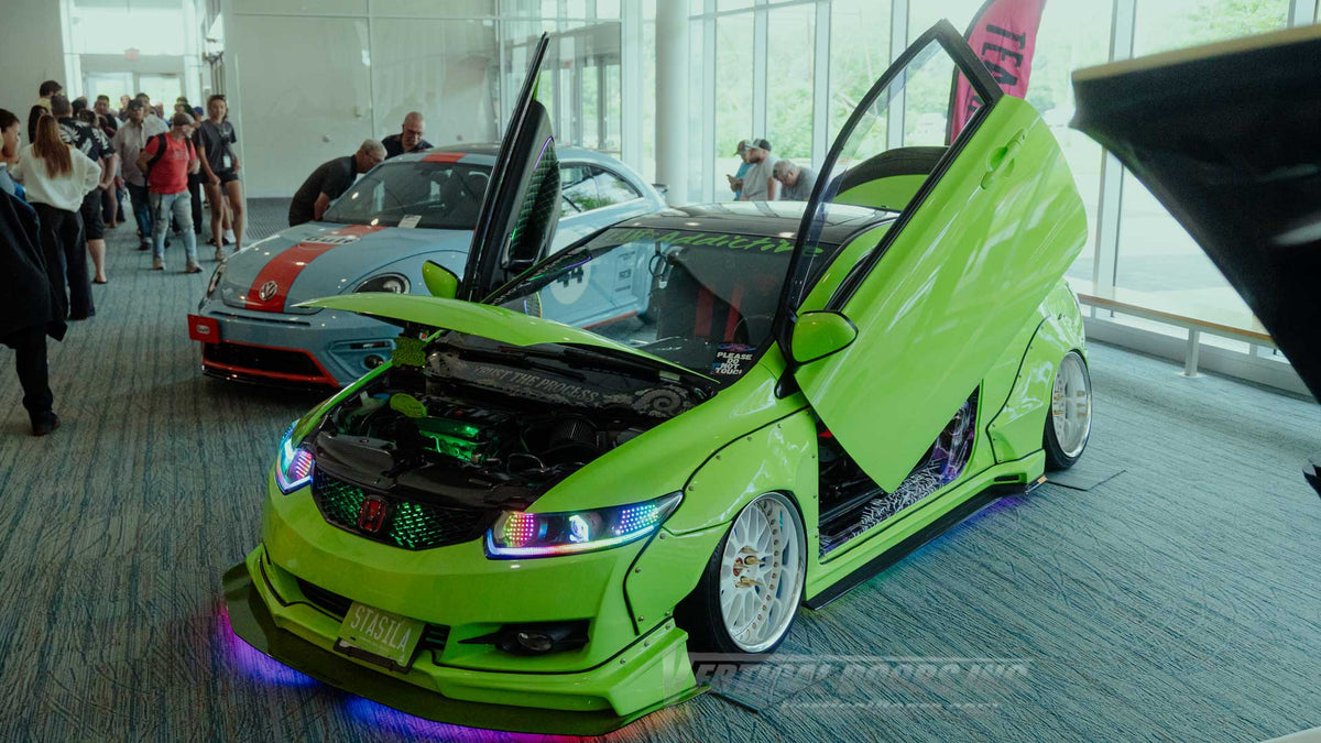Kyle’s 2008 Honda Civic LX coupe displayed indoors with both vertical doors raised, an open hood, RGB headlights, widebody flares, and multicolor underglow. - VDCHC06082D